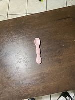 Top side view of a small pink children's eating spoon placed on a wooden surface showing the textured grip handle and the spoon bowl.