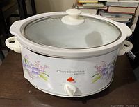 Full view of the white Continental Electric crock pot with floral decals and glass lid on a wooden surface.