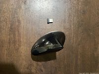 Black ergonomic handheld wireless mouse with contoured shape and glossy finish, placed next to small USB receiver on wooden surface.