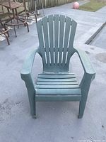 Front view of green plastic lawn chair on concrete ground showing slatted back and seat with integrated armrests