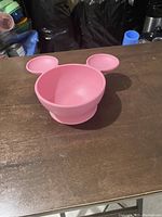 Front view of pink Minnie Mouse shaped bowl with 3 bowl sections (1 large, 2 ears) on wooden surface.