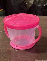 Front and side view of the pink plastic snack bowl with curved handles, heart cutout, and tight fitting lid with dispensing slits.