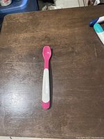 Top-down view of a pink and white plastic baby feeder spoon on a wooden surface.