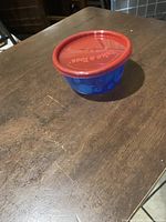 Small blue bowl with red lid closed, on wood table