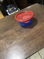 Small plastic Take & Toss bowl on wooden table, blue base with polka dots and red lid.