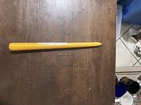 Photo of a single tall yellow taper candle laying horizontally on a wooden surface.