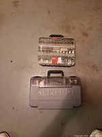 Photo showing two plastic cases: one gray hard case for the main Dremel tool and one clear plastic case with many accessory compartments and bits inside.
