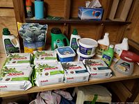 Overview photo of all gardening products including fertilizer spike packages, bottles of horticultural oils, and sprayer attachment on wooden shelf