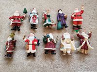 Photo of 11 Hallmark Santa Claus ornaments with various international designs, laid out in two rows on carpet.