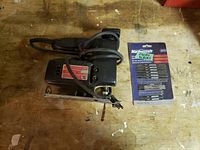 Top-down view of the black electric jigsaw and the unopened Mastercraft jigsaw blades package on a wooden surface.