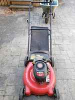 Front view of red Yard Machines lawn mower with black handlebar and rear grass collection bag.