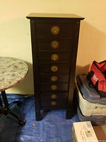 Front view of tall lingerie chest showing all eight drawers with brass pull handles, dark brown finish, and adjacent furniture pieces.