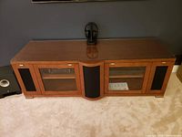 Front view of wood media console cabinet with glass doors and fabric speaker panels, showing top, front and sides.