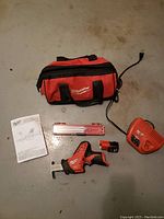 All items laid out on floor: saw, battery, charger, manual, and carry bag.