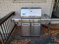 Front view of Weber Genesis natural gas grill showing stainless steel body, side shelves, and cabinet doors