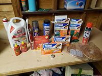 Wide shot showing full lot on wooden table with Ortho Home Defense Max 4L container, multiple Terro ant bait liquid boxes, ant poison spray, wasp killer spray, critter repellent, and wasp nest decoys.