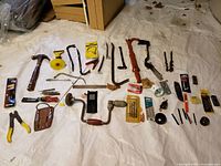 Overview of all tools laid out on a white tarp, showing hammer, pry bars, hand drill, wire strippers, blades, and drill bits.