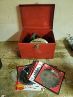 Photo showing red metal box containing the Skil circular saw and several saw blades laid out in front of the box.