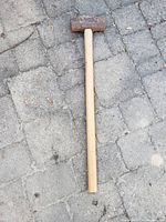 Full view of the sledge hammer showing wooden handle and metal head on pavement.