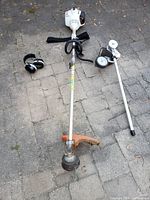 Overview of all lot items laid out on pavement: Stihl brush cutter, edger attachment with wheels and spool, ear protection earmuffs.