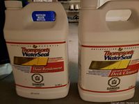 Two full unopened white jugs of Thompson's Water Seal showing front labels: Multi-Surface Waterproofer and Heavy Duty Deck Cleaner, both 3.78 liters.