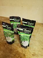 Four unopened bags of white clover seed displayed on a wooden surface.