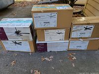 Six boxed ceiling fans stacked outdoors on pavement