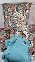 Photo showing four paisley decorative pillows and folded teal curtains with grommets