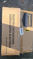 Photo of the closed cardboard box labeled Greenworks Electric Dethatcher with product and brand details.