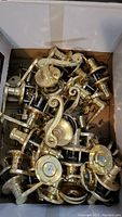 Box containing multiple gold-colored door handles with different styles including curved lever handles and round knobs. Handles show used wear and tarnish.