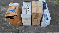 Photo showing six cardboard boxes with various labels including a Channel Master Feeder-Pak box, stacked outside on pavement.