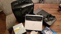 Photo showing Fellowes paper shredder, Neat scanner, HP DeskJet 1000 printer, three DVD drives, and Valiant iron on chair and floor.