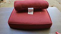Photo showing stacked chili red patio seat and back cushions with visible fabric texture and label.