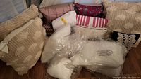 Photo showing collection of assorted pillows and pillow covers in various patterns and colors on floor.