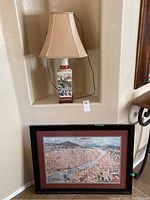 Porcelain table lamp with Asian bird and floral design next to Italian-themed framed cityscape art print.