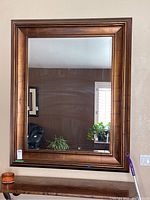 Front view of the large rectangular wall mirror with wooden frame hung on wall, showing clear reflection and polished wooden border.