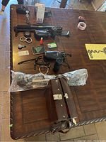 Photo showing assorted camera lenses, carrying case, camera stand, light meters, and accessories on a wooden table.