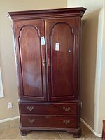 Front view of Ethan Allen wooden armoire with closed panel doors and brass drawer handles.