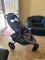 Full view of gray Evenflo stroller with sun canopy, cup holder, and three wheels in indoor setting.