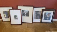 Five framed watercolor prints leaning against a wall, showing a range of scenes and sizes with wood grain frames.