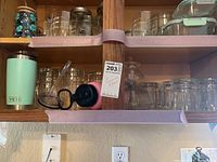 Shelf with light blue Yeti tumbler, black lid straw top, various clear rocks glass and travel cups, a glass canister with lid on top shelf.