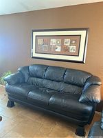 Front view of black leather couch showing three seat cushions and padded arms with 8-inch risers