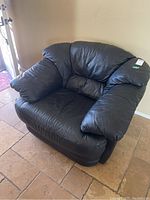 Front-right angle view of the black leather living room chair showing plush armrests and cushioned seat and back.