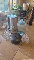 Photo of kitchen items including black cast iron Lodge dutch oven with lid, glass drink dispenser, stainless steel coffee pot, plastic cups, Pyrex baking dishes, and stainless steel trash can.