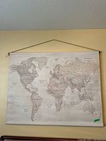 Canvas world map printed in neutral tones with geographic details, hanging on wall by string.