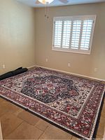 Photo of the Ruggable washable rug laid flat on tiled floor with visible traditional medallion pattern in red, black, beige, and white colors.