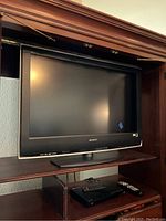 Sony Bravia television placed inside a wooden entertainment unit with remote controls and a device underneath.