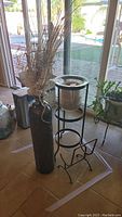 Photo showing tin vase with faux branches next to metal frame candle holder on a tiled floor in front of glass doors.
