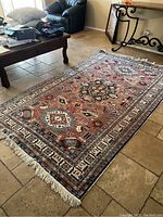 Full view of the vintage Persian area rug laid flat on a tiled floor, showing overall design and condition with fringe on one short side.