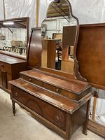 Front angle view of antique wooden dresser showing details of drawers, legs, and mirror frame.